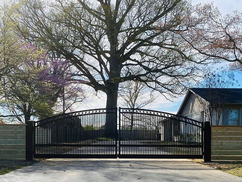 A black gate is leading to a house with trees in the background.