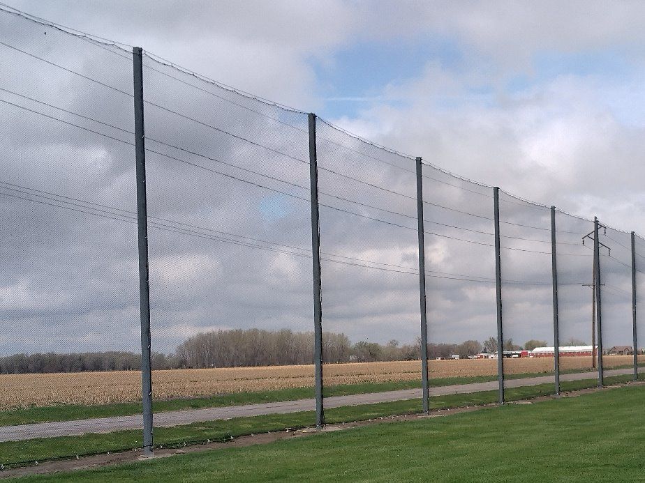 A chain link fence surrounds a grassy field on a cloudy day