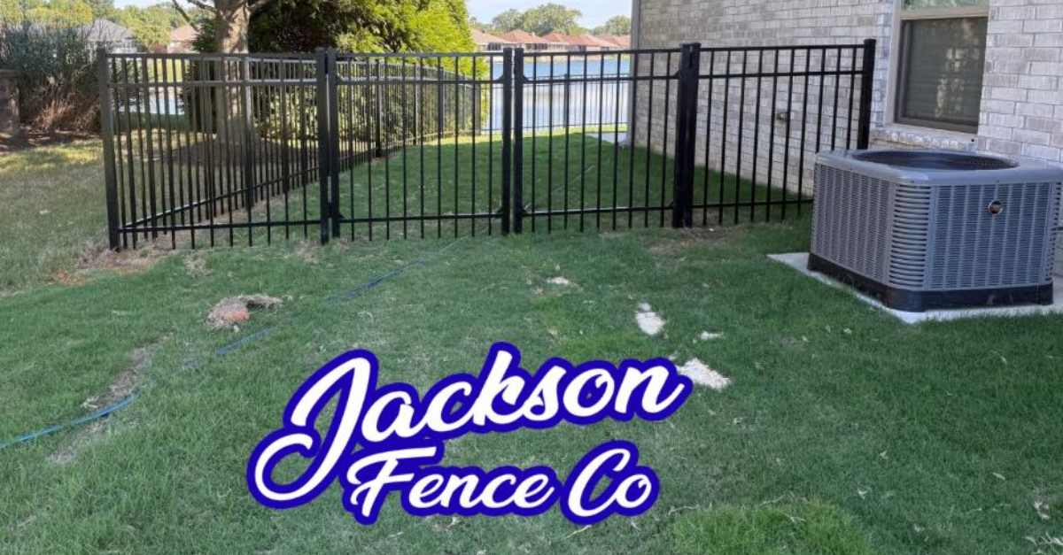 Black metal fence in a yard next to a building and air conditioning unit with the logo for Jackson Fence Co.