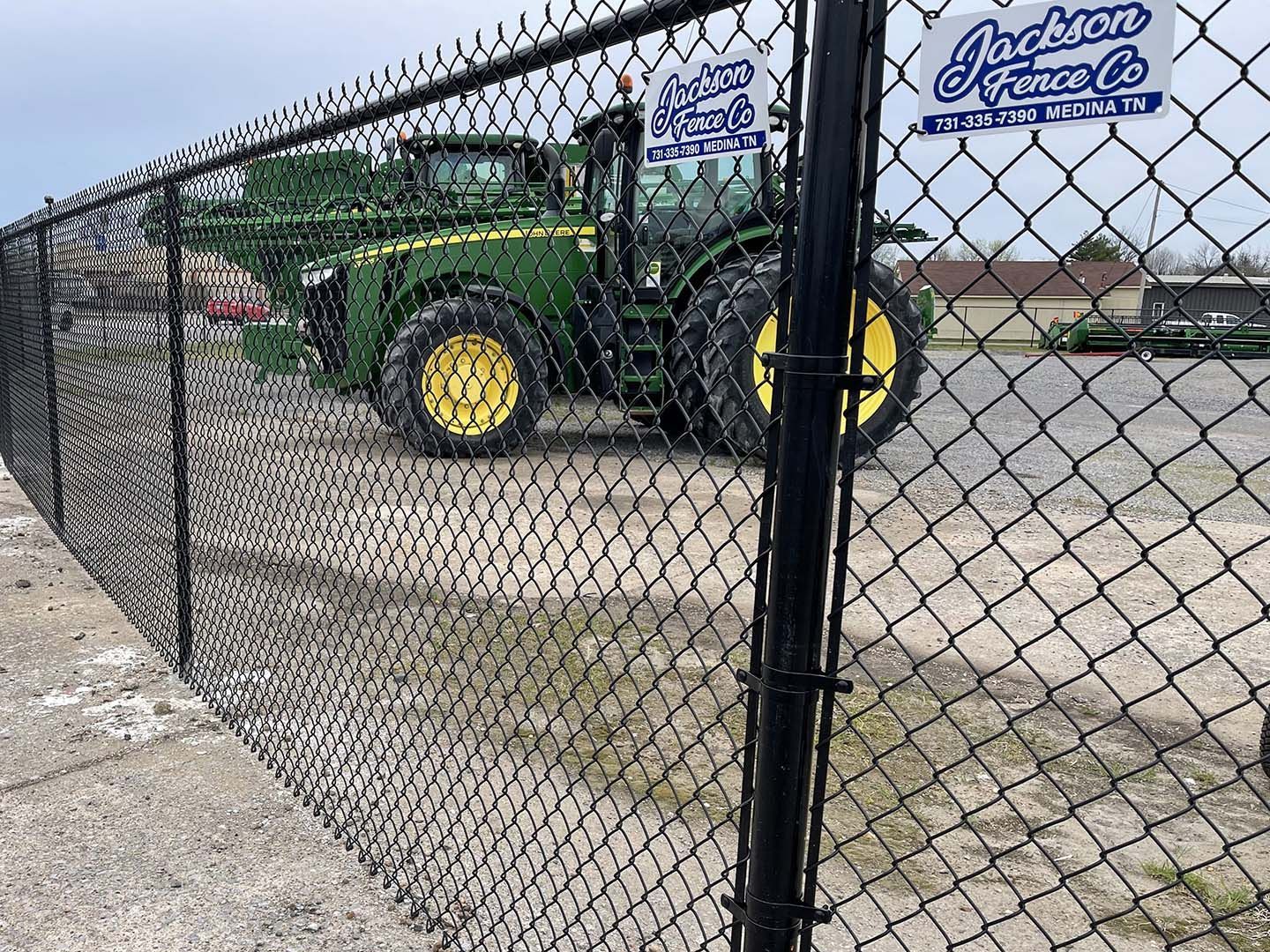 A green tractor is parked behind a chain link fence.