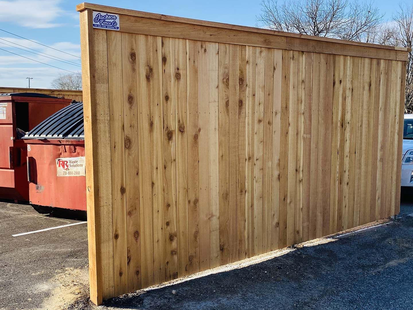 A wooden fence in a parking lot with a dumpster in the background