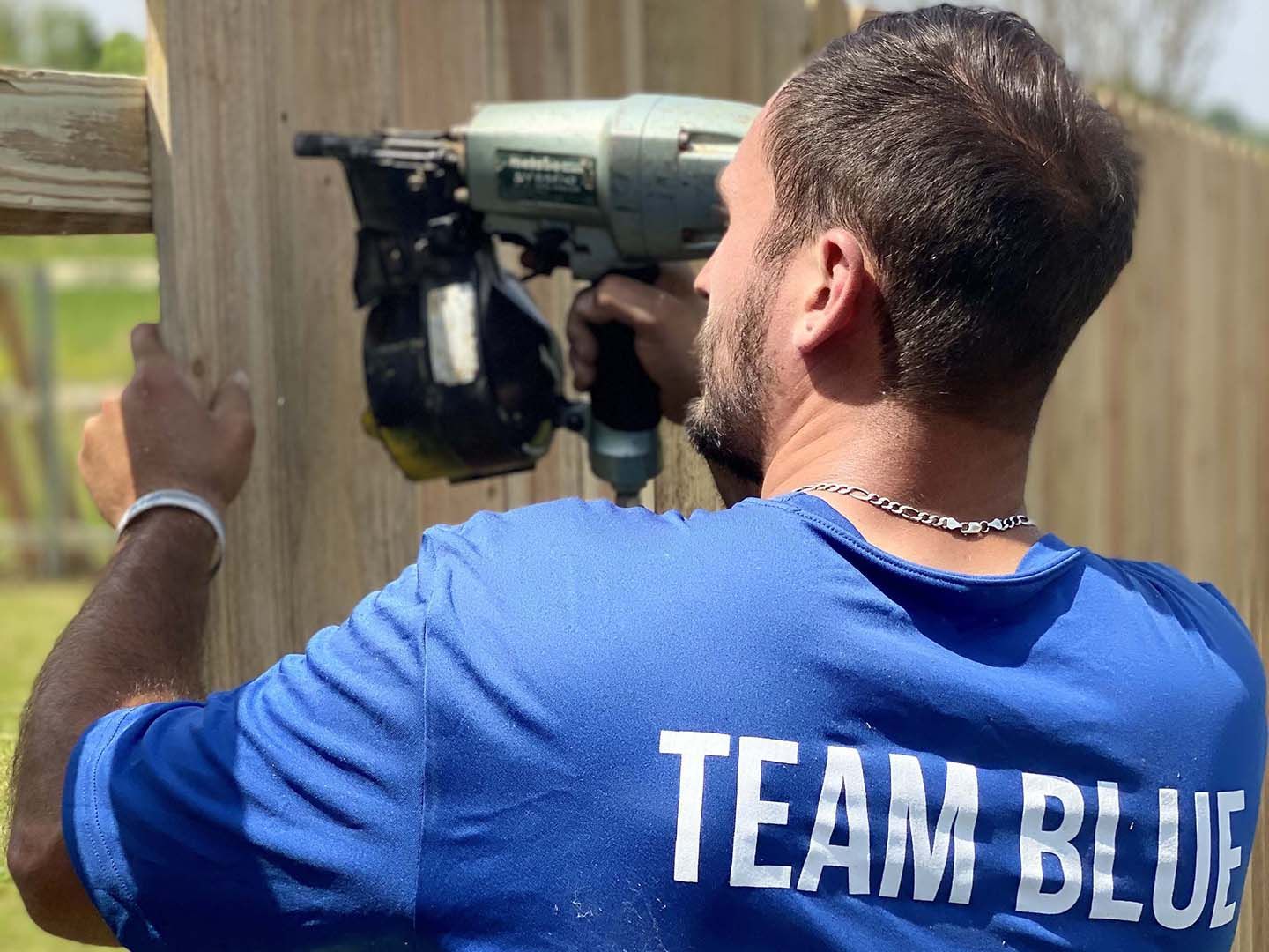 Man wearing Team Blue shirt working on a wood fence