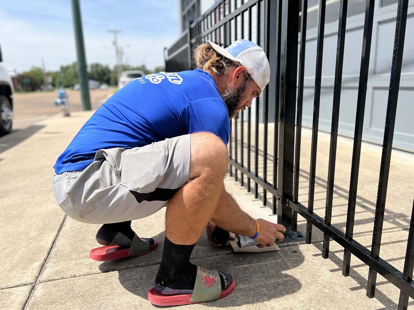 A man is squatting down to fix a metal fence.