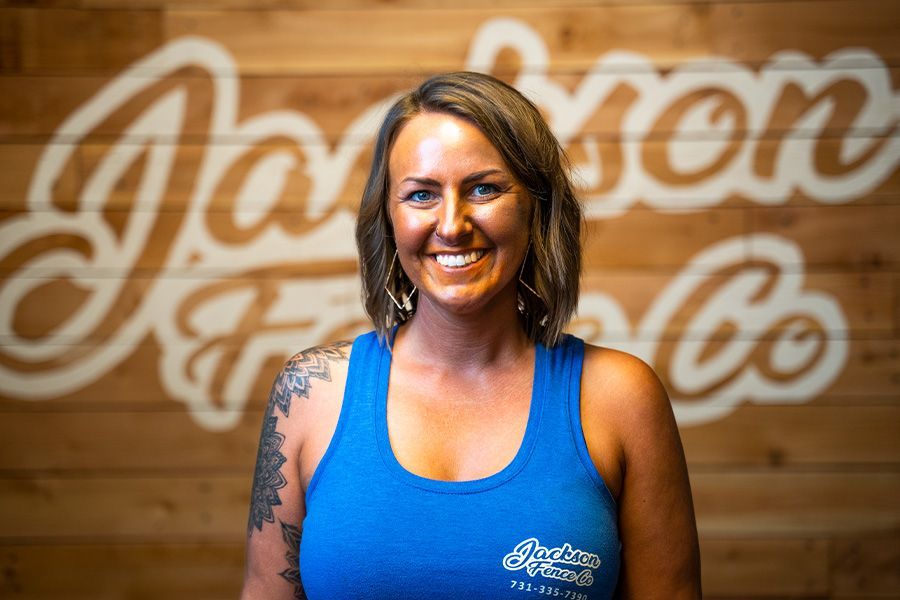 A woman in a blue tank top is smiling in front of a wooden wall.