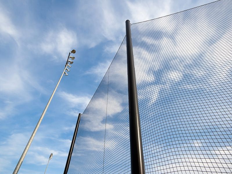 Looking up at a baseball net with a blue sky in the background.