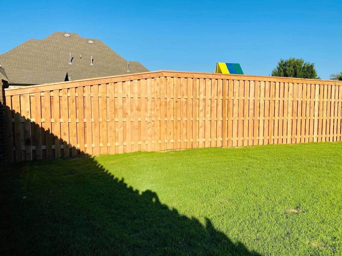 A wooden fence surrounds a lush green yard with a house in the background.