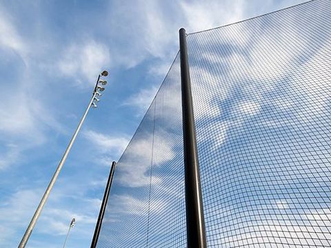 A close up of a baseball fence with a blue sky in the background.