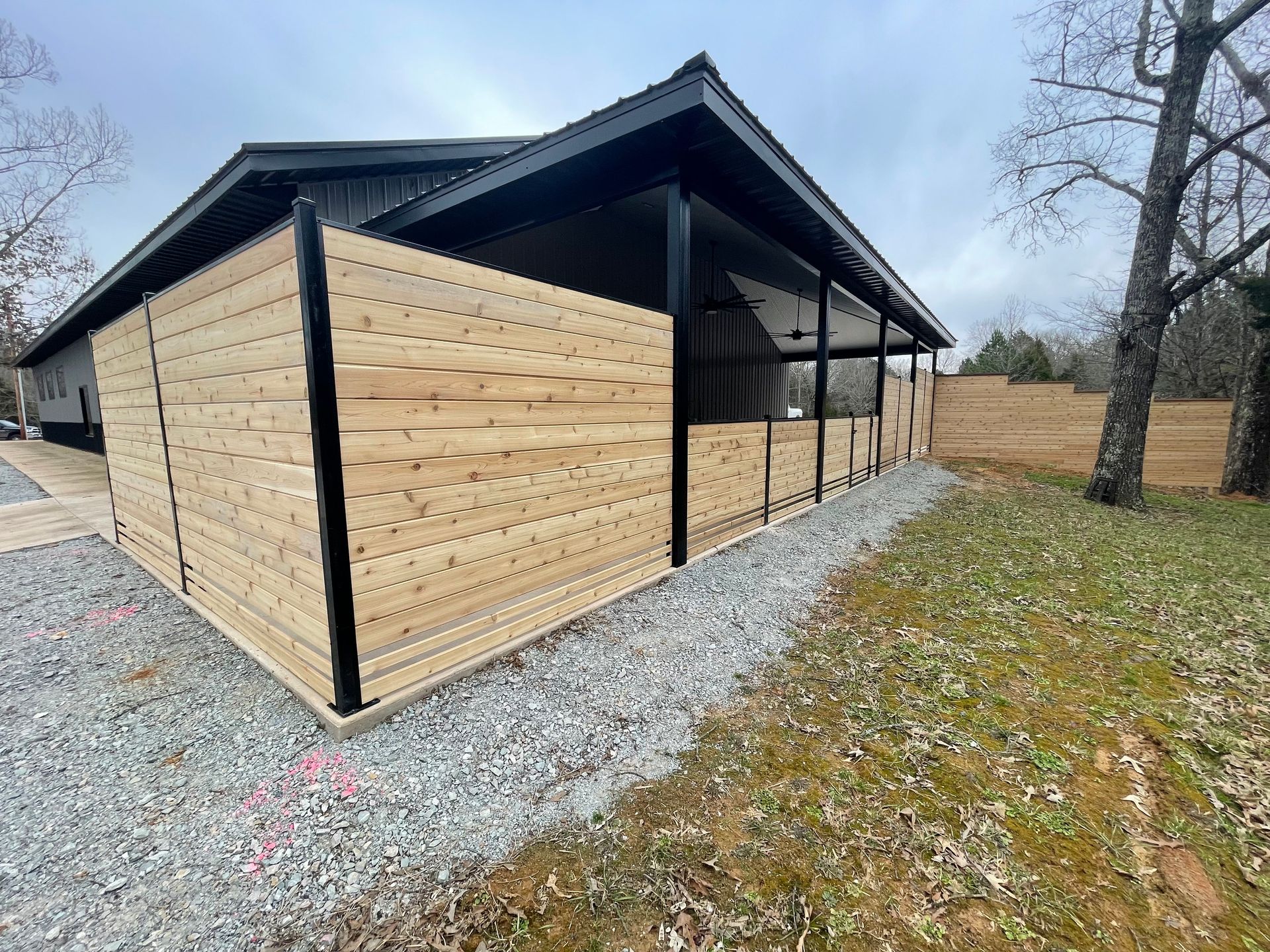 Wooden fence surrounding a covered outdoor area with gravel and grass in a cloudy setting.