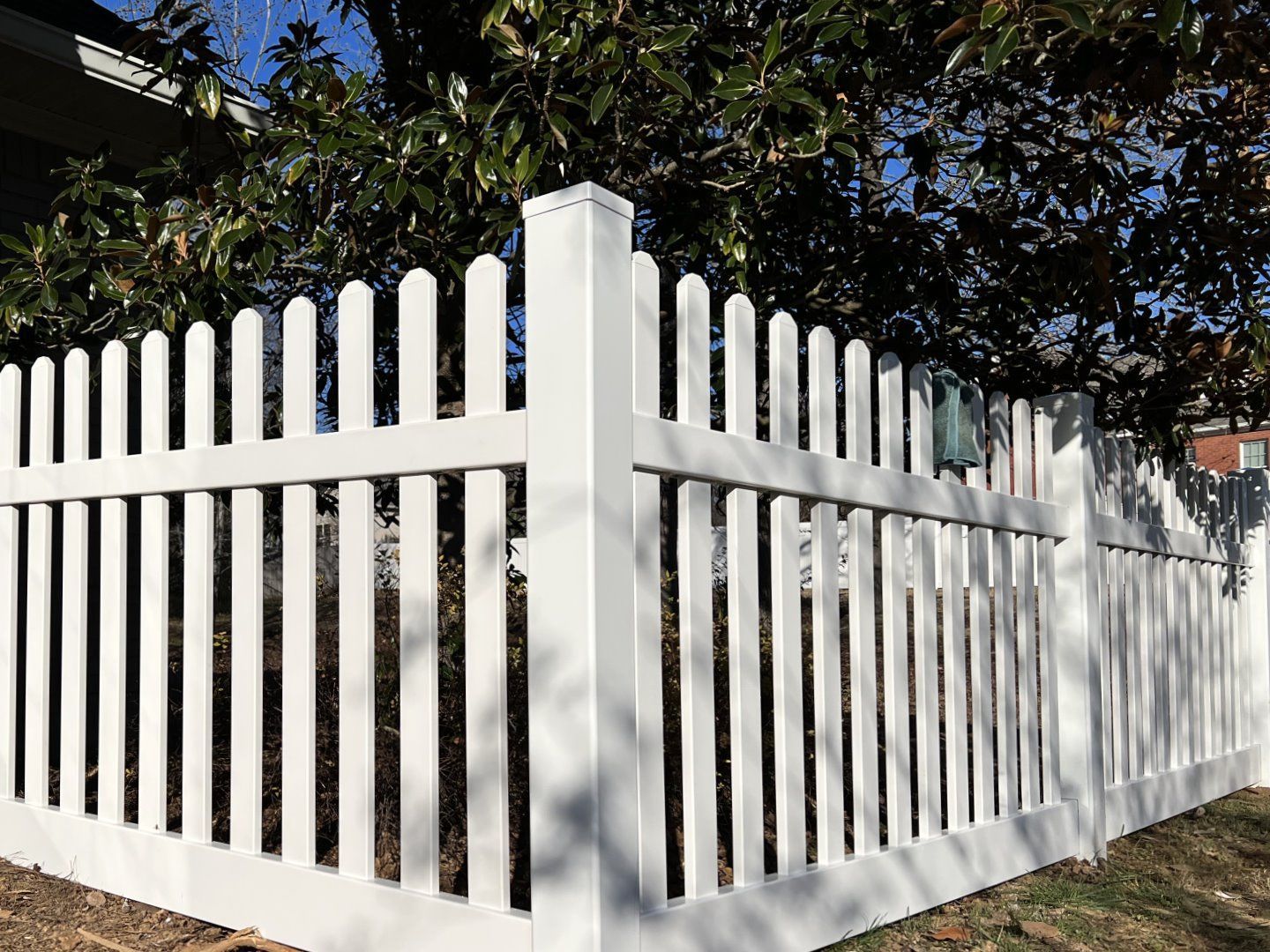 A white picket fence is surrounded by trees in front of a house.