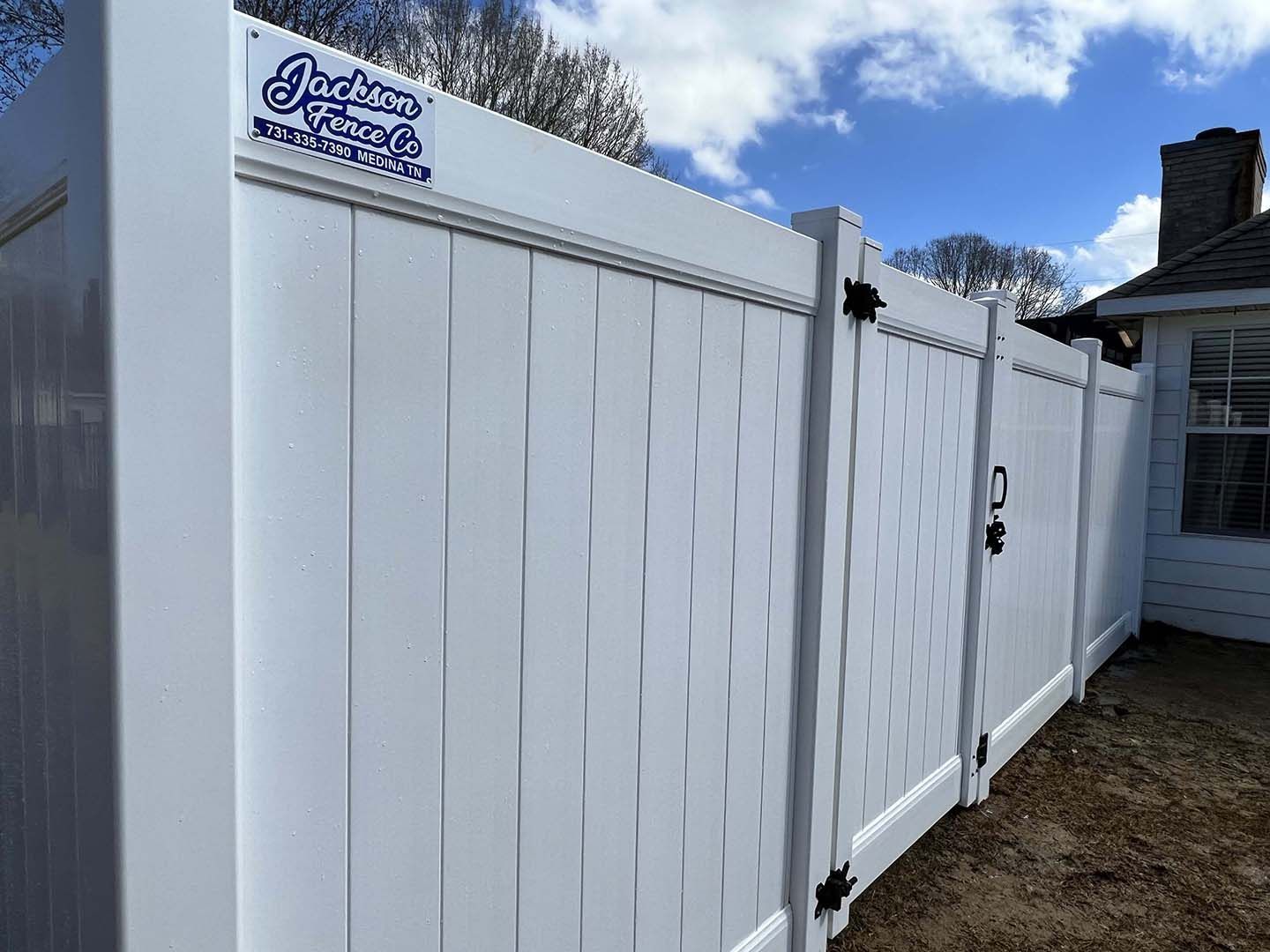 A white vinyl fence with a gate in the backyard of a house.