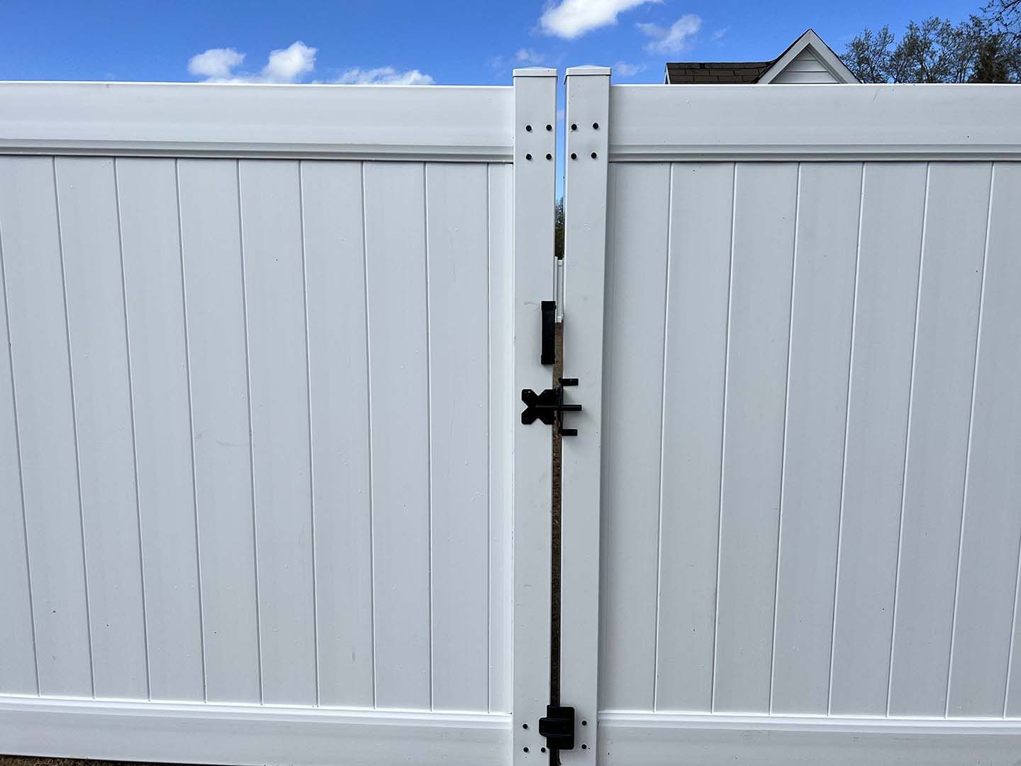A white fence with a black gate and a blue sky in the background.