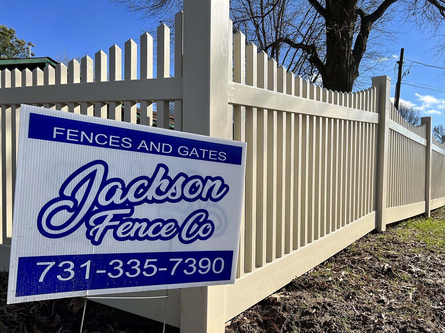 A sign for jackson fence co. is sitting next to a white fence.