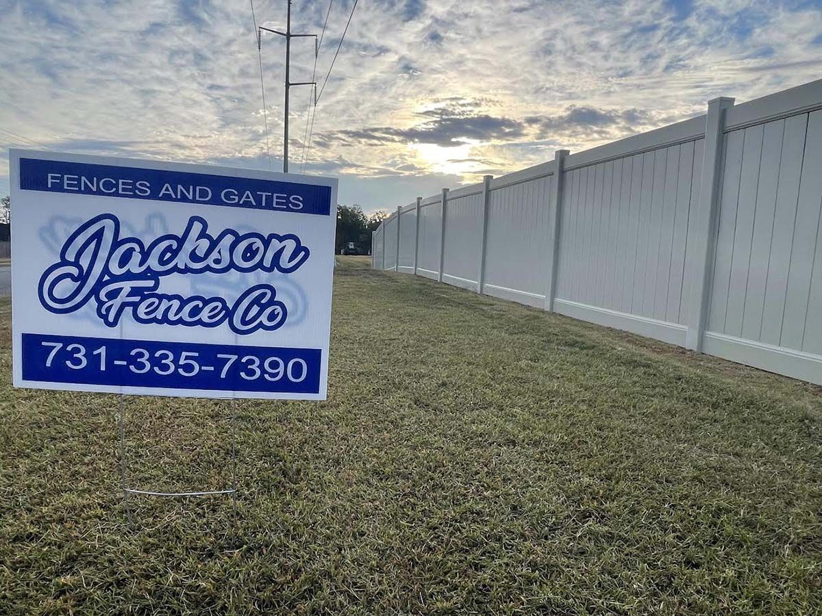 A sign for jackson fence co. is sitting in front of a white fence.