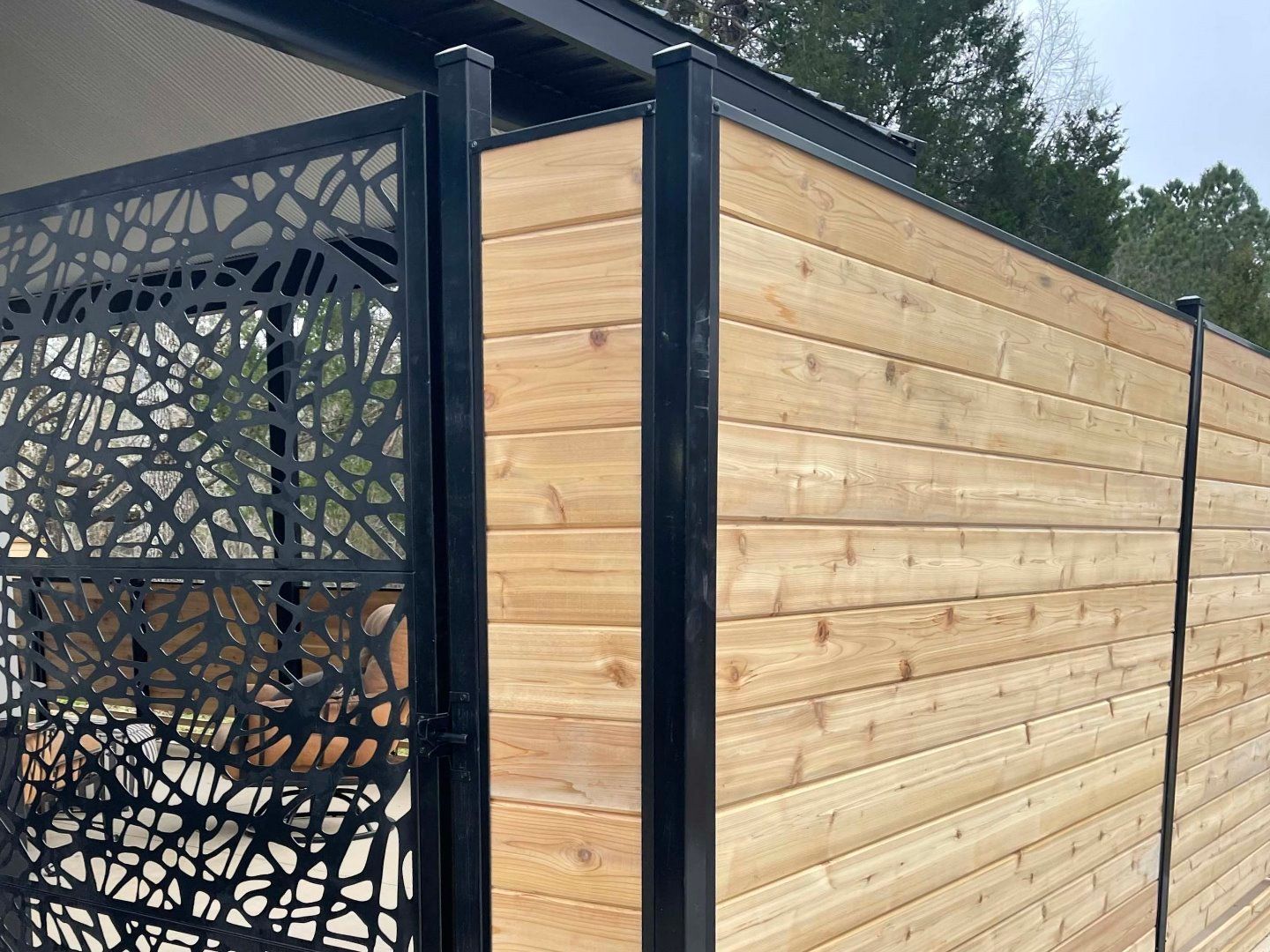 A wooden fence with a black metal fence in front of a house.