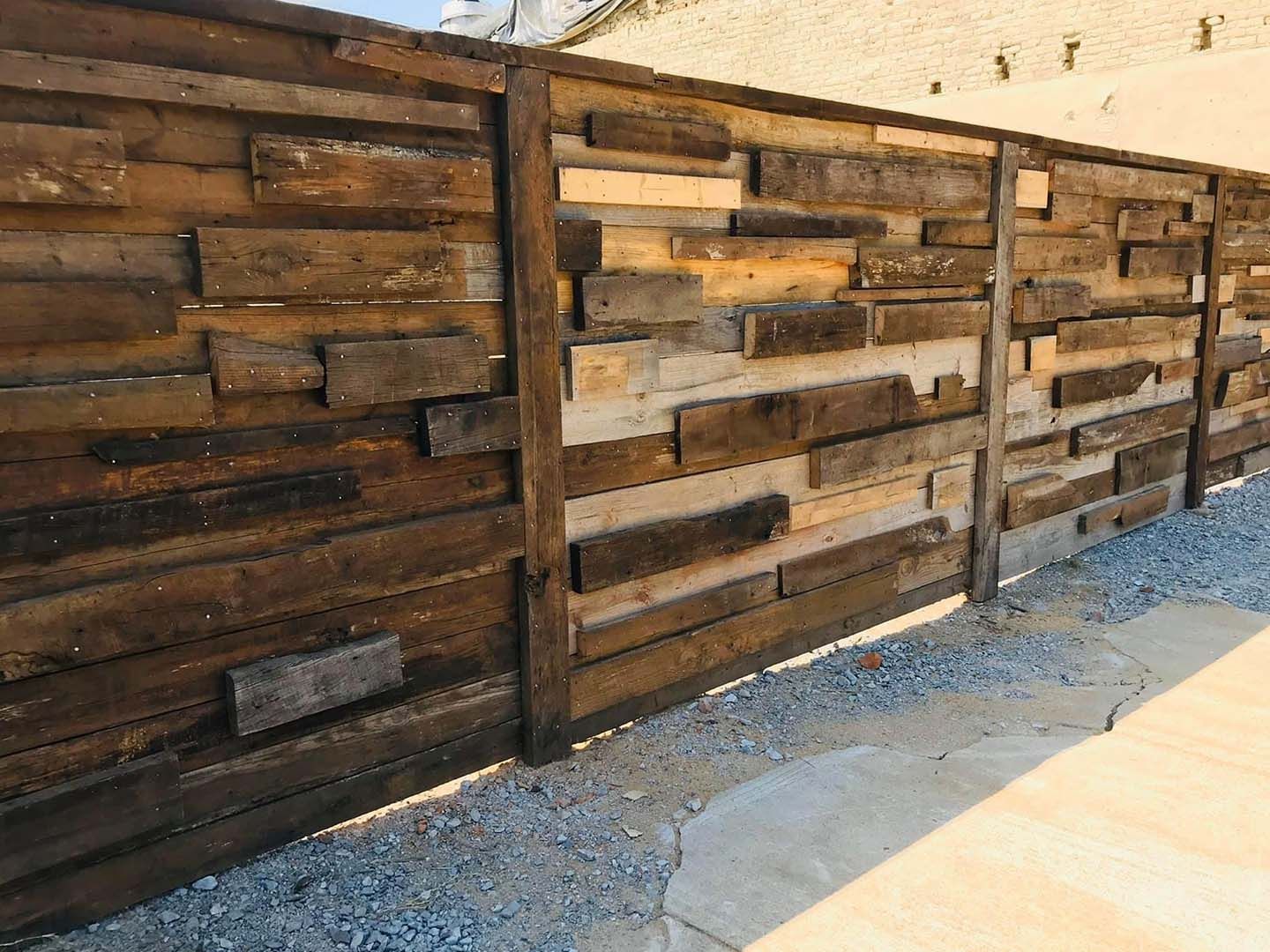 A wooden fence made of wooden boards is sitting next to a gravel path.