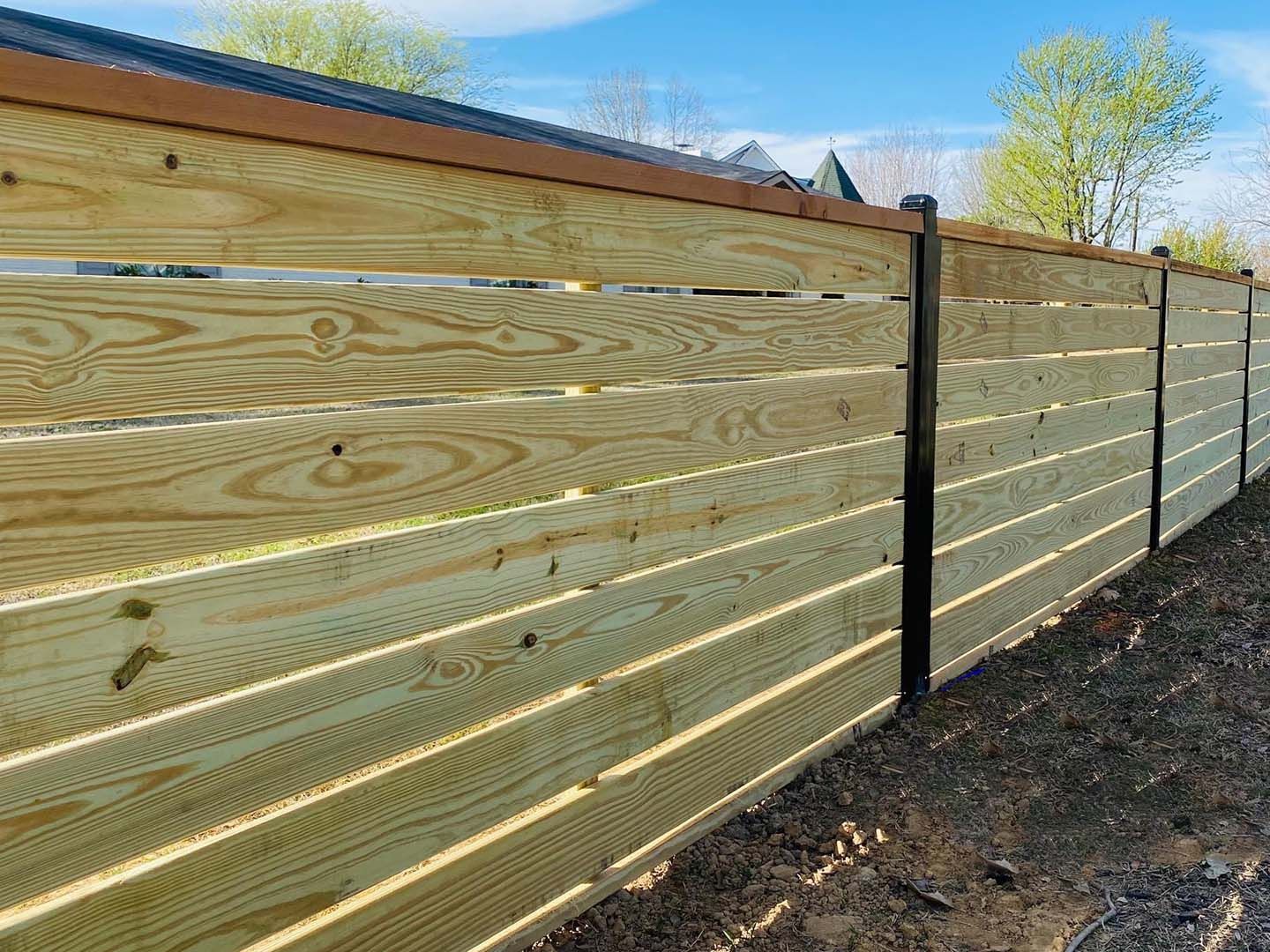 A wooden fence is sitting on top of a dirt field next to a house.