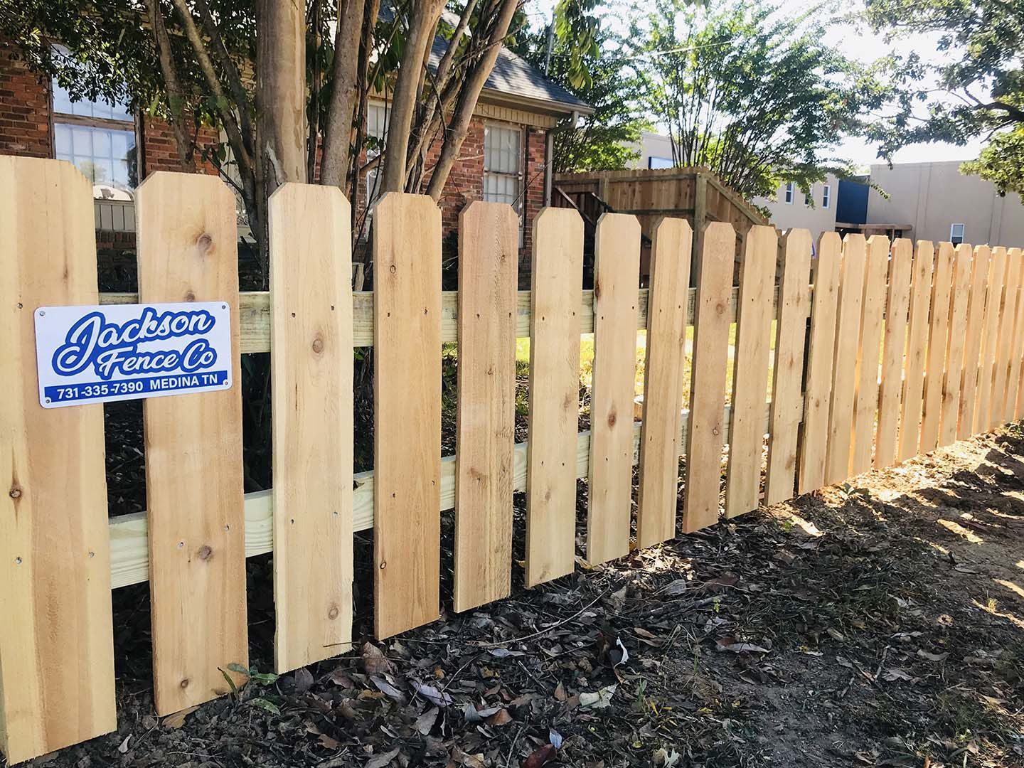 A wooden picket fence with a sign on it in front of a house.