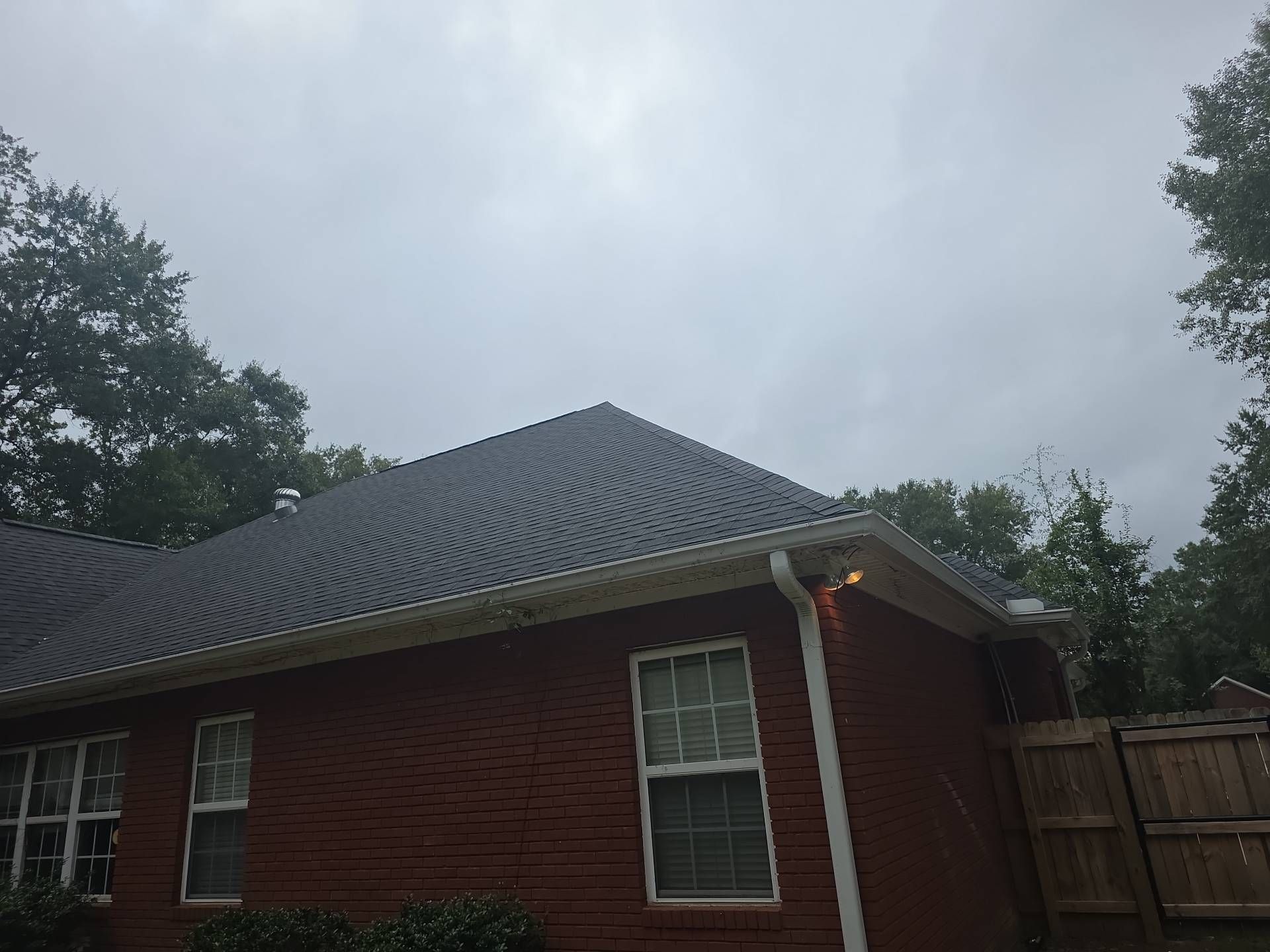 Brick house with dark roof and white gutters under a cloudy sky.