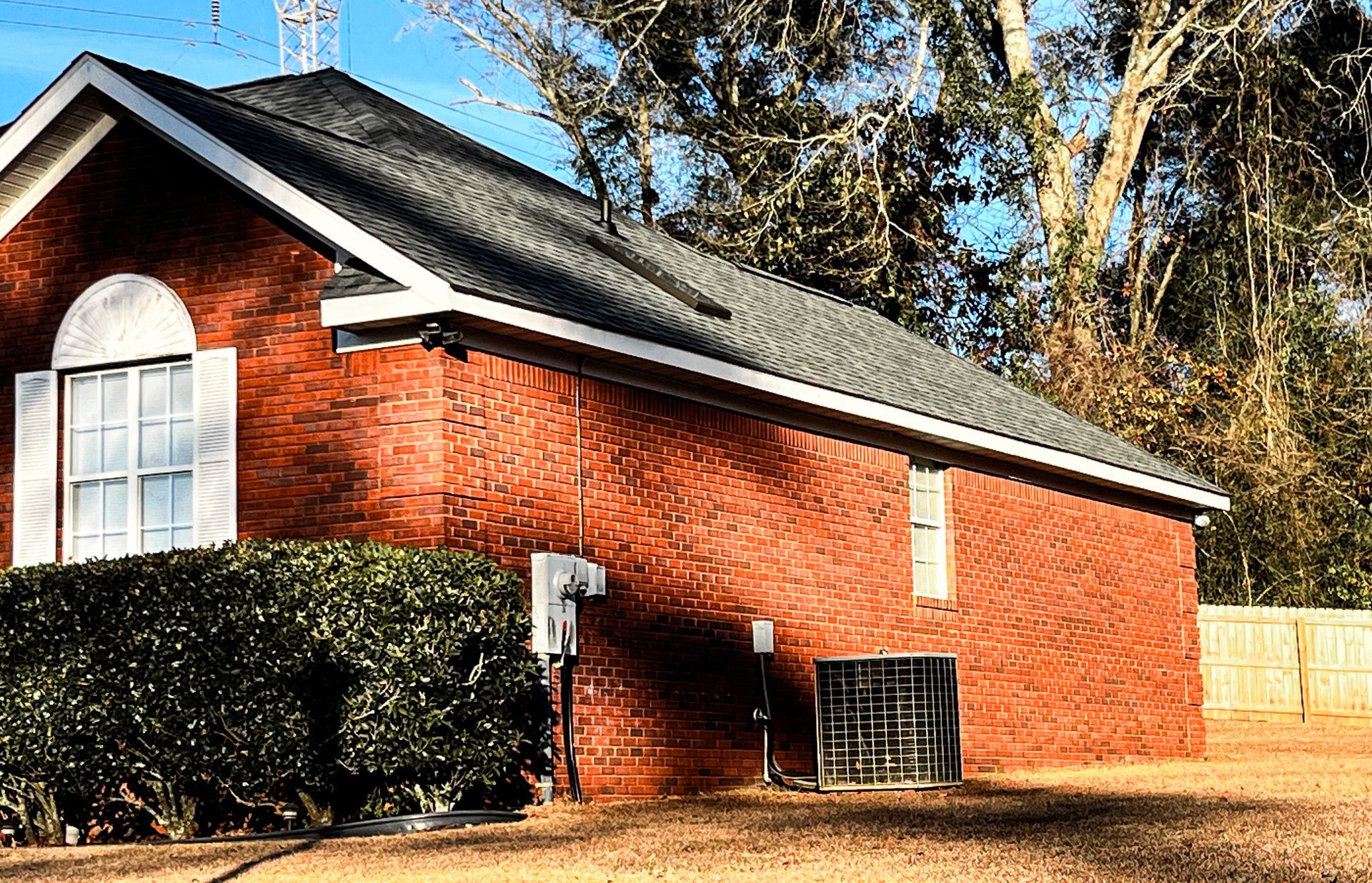 Brick house with black roof, white trim, and air conditioning unit.