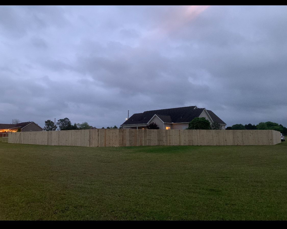 Wooden fence surrounding a house on a grassy lawn under a cloudy sky.