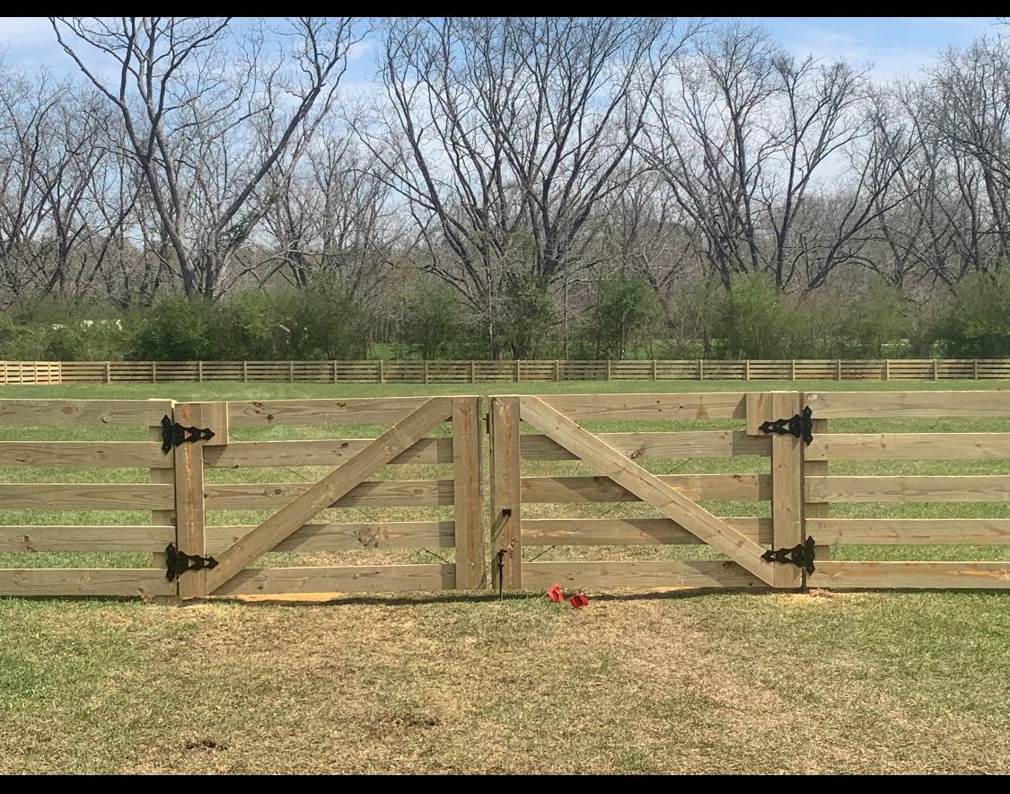 Wooden farm gate in a field, with a forest background.