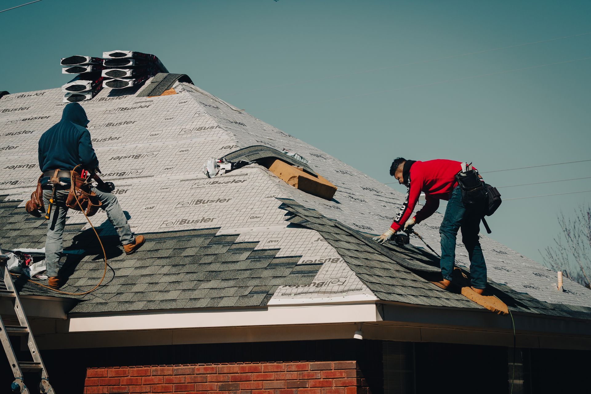 Two roofers install shingles on a house roof on a sunny day.