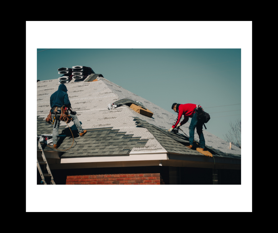 Two roofers installing shingles on a house roof on a sunny day.