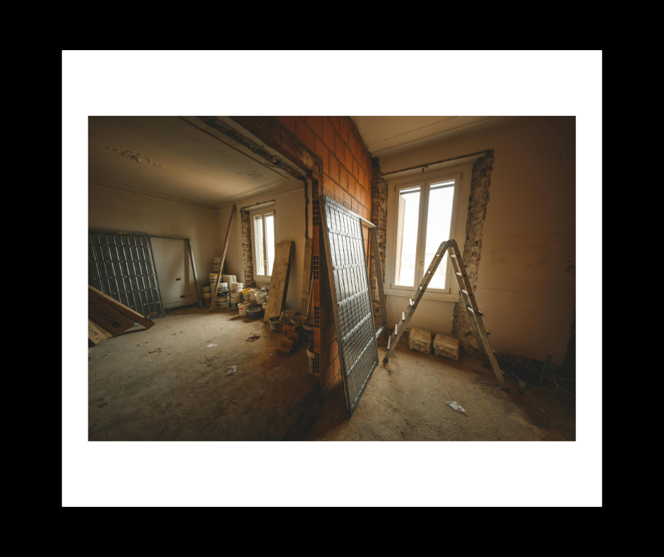 Room under renovation, exposed brick, ladder, and debris. Bright window in background, unpainted walls.