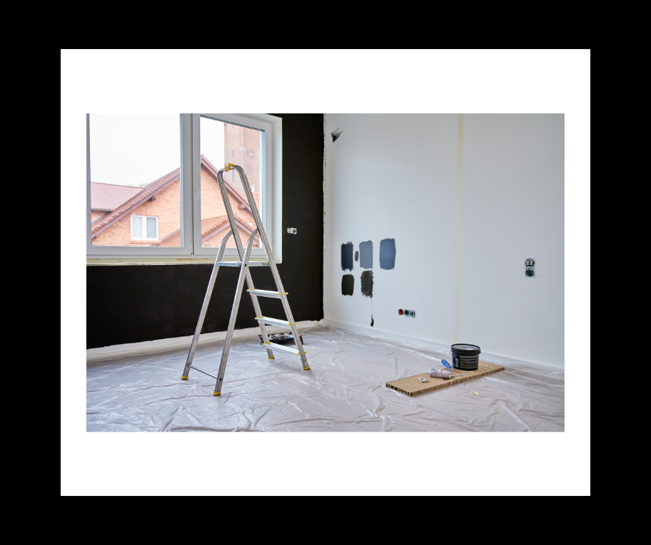 Interior room during renovation; ladder, drop cloth, two-tone walls (black and white), paint swatches.