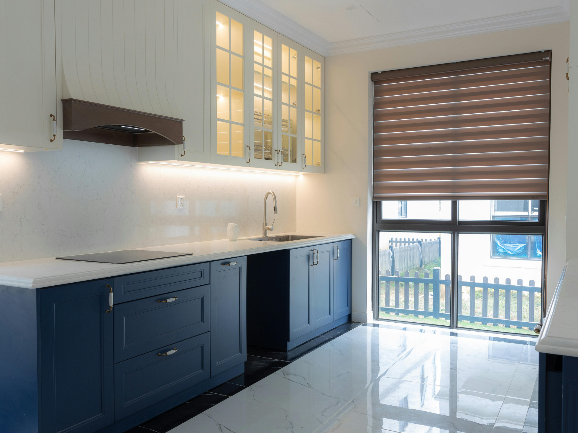Modern kitchen with navy cabinets, white counters, glass-front uppers, and a sliding door with blinds.