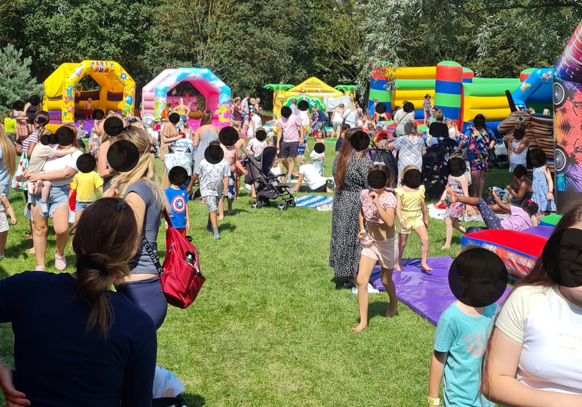 A large group of people are playing in a park with bouncy houses.