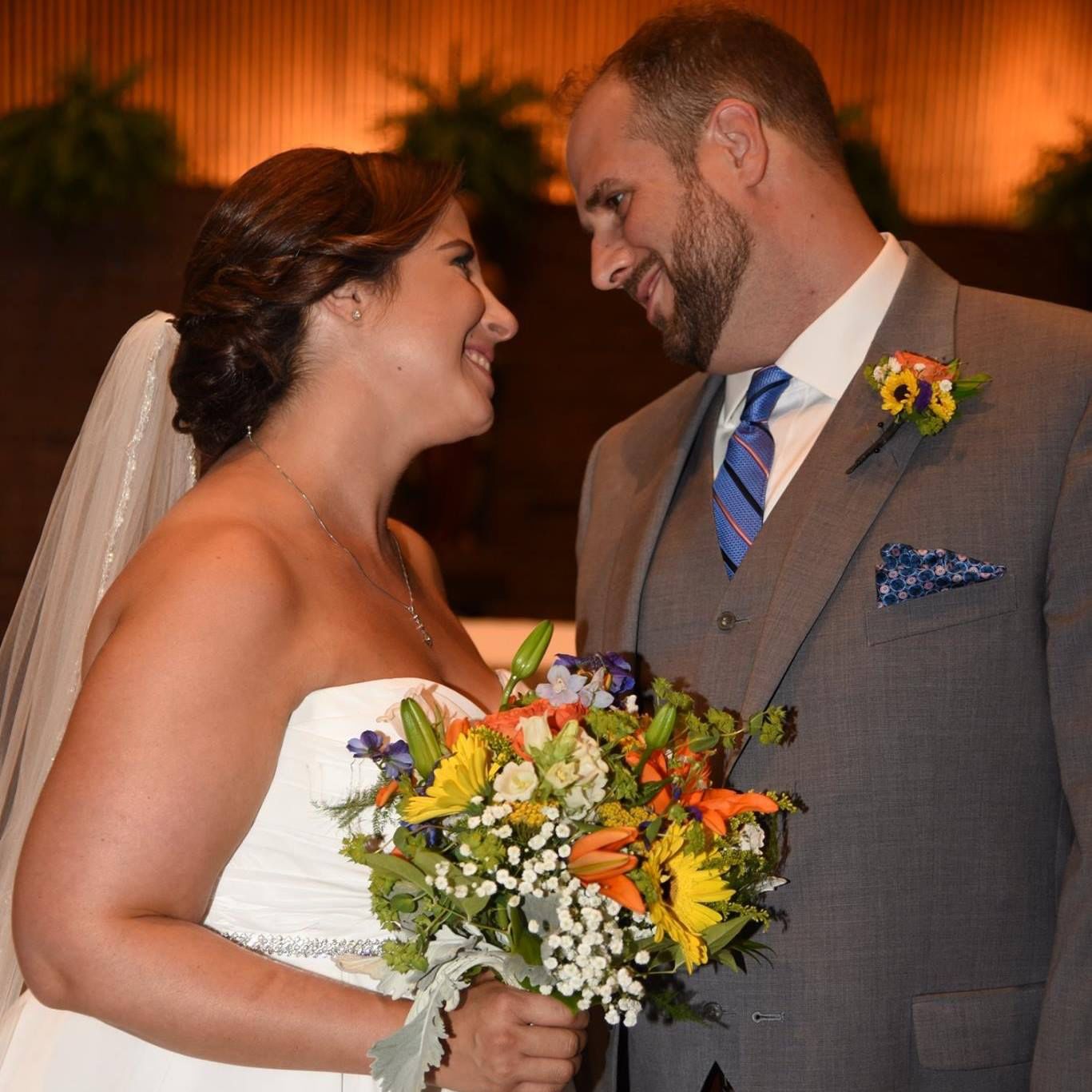 A bride and groom are looking at each other and the bride is holding a bouquet of flowers