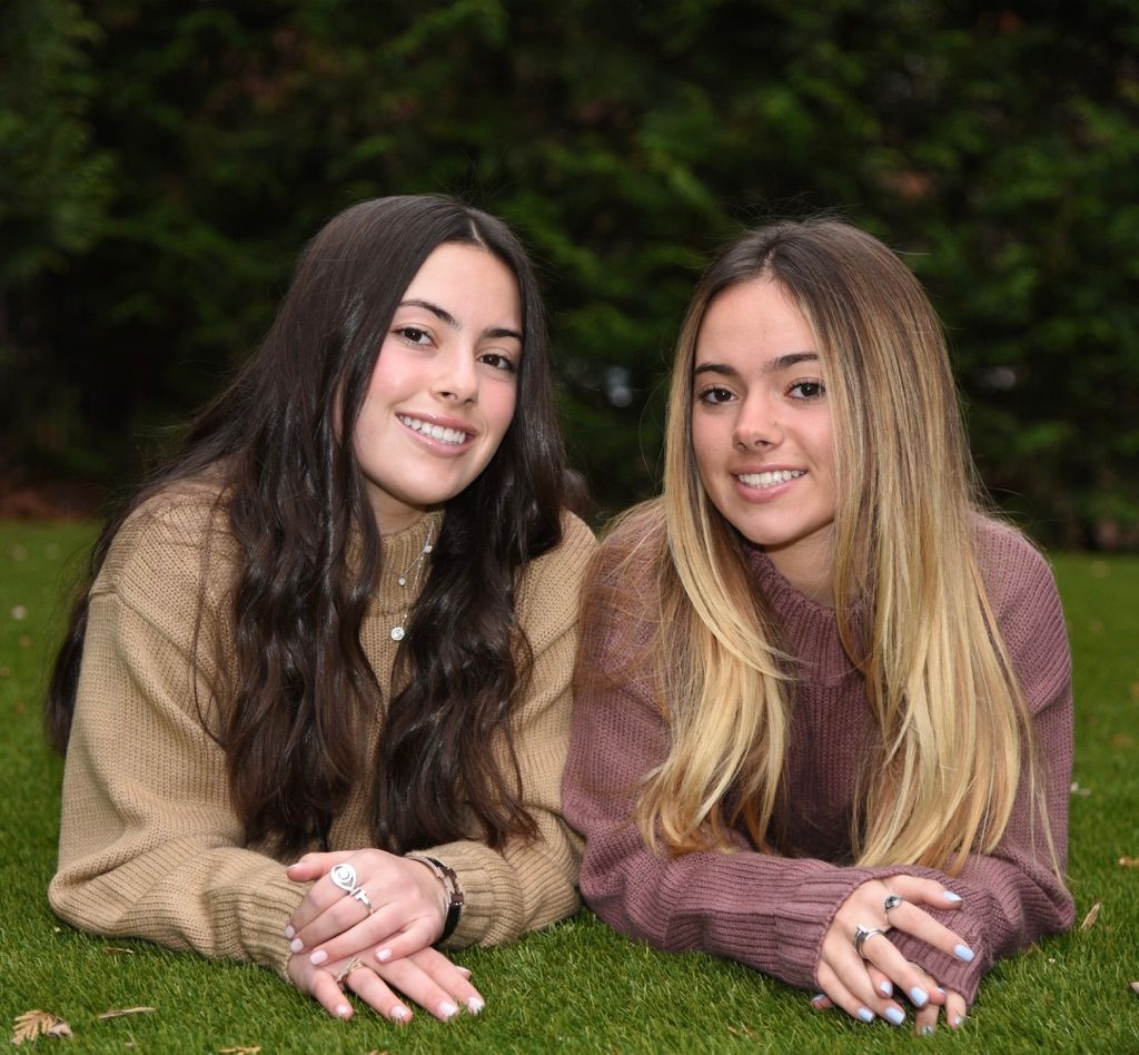 Two young women are laying on the grass and smiling for the camera.