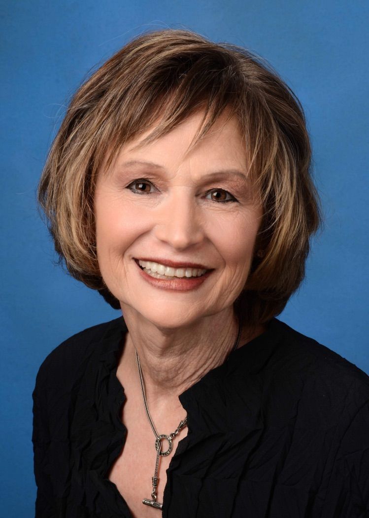 A woman wearing a black shirt and a necklace is smiling for the camera.