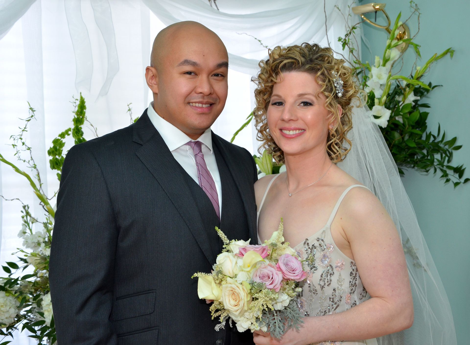 The bride and groom are posing for a picture and the bride is holding a bouquet of flowers