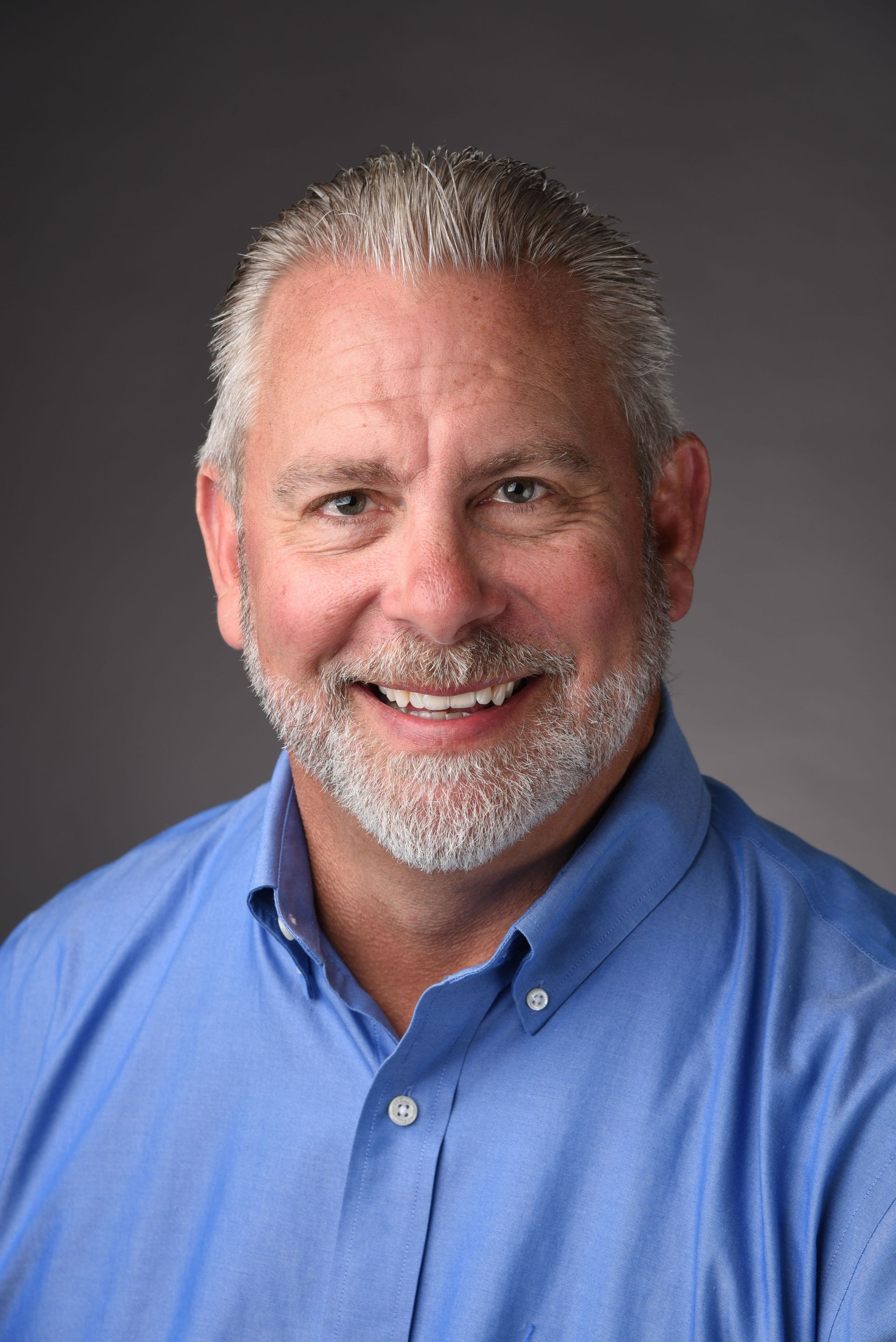 A man with a beard and a blue shirt is smiling for the camera.