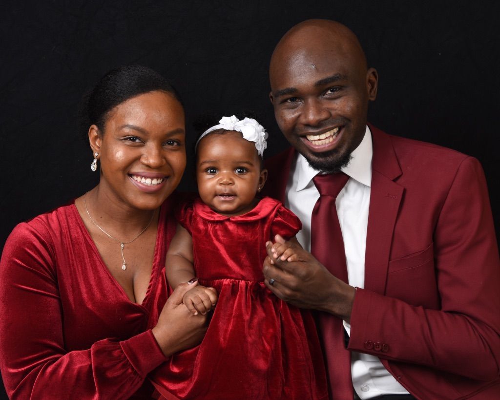 A man and woman are posing for a picture with a baby in a red dress.