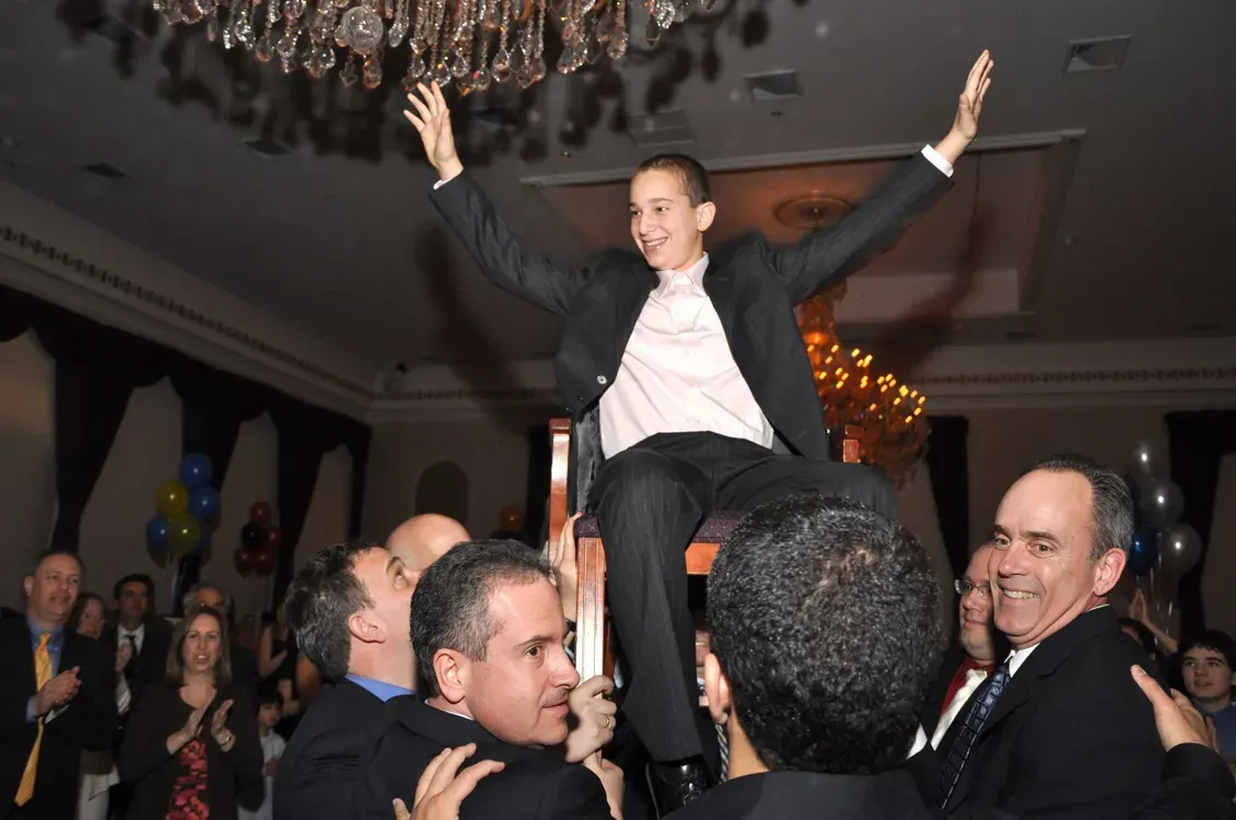 A boy in a suit is being lifted in the air by a group of people