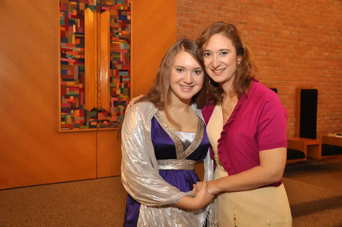 Two women are posing for a picture in front of a brick wall.