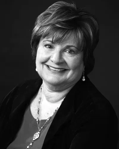 A black and white photo of a smiling woman wearing a necklace and earrings.