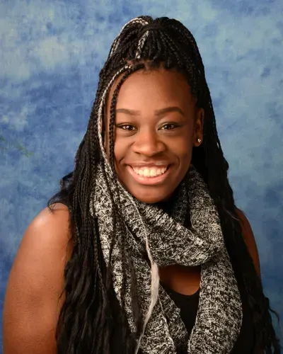 A woman wearing a scarf and braids smiles for the camera