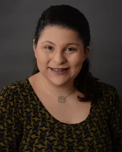 A woman wearing a necklace and a green shirt is smiling for the camera.