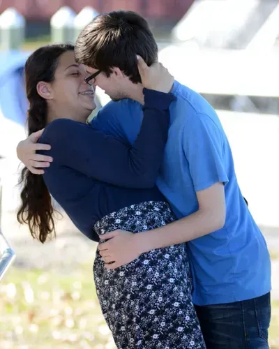 A boy in a blue shirt is holding a girl in his arms