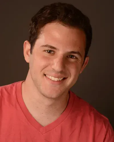 A young man in a red shirt is smiling for the camera.
