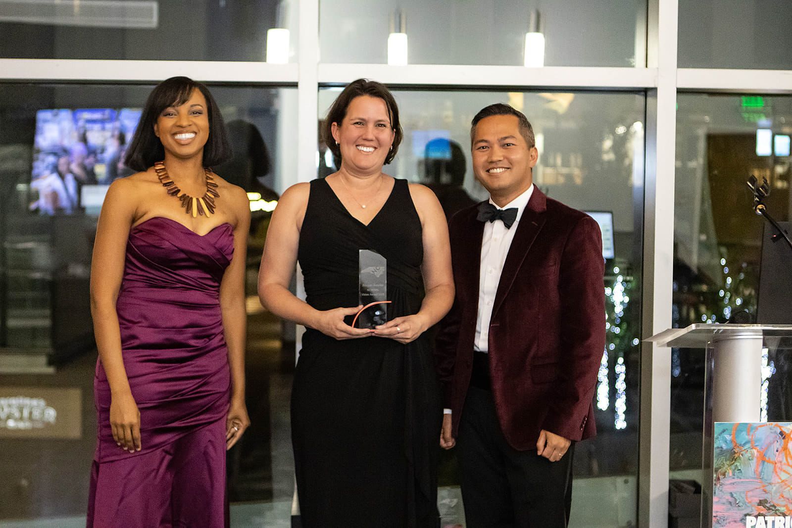 Three people are standing next to each other in front of a window holding awards.