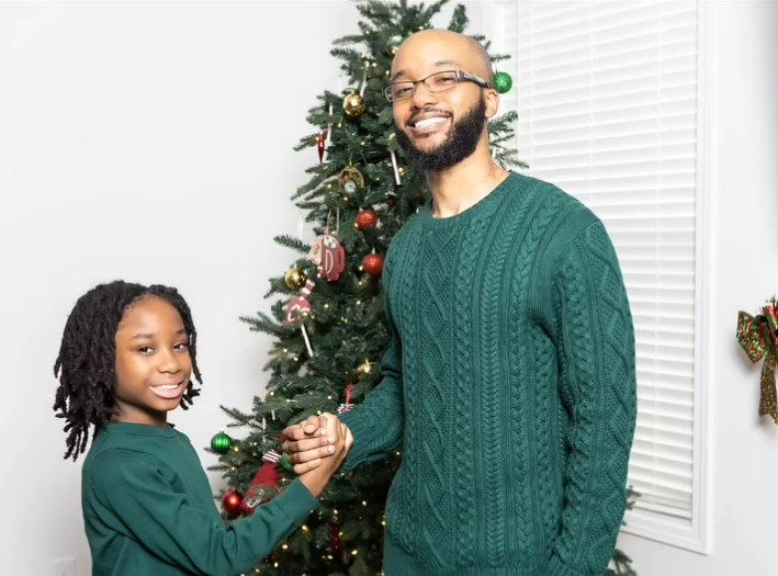A man and a girl are shaking hands in front of a christmas tree.