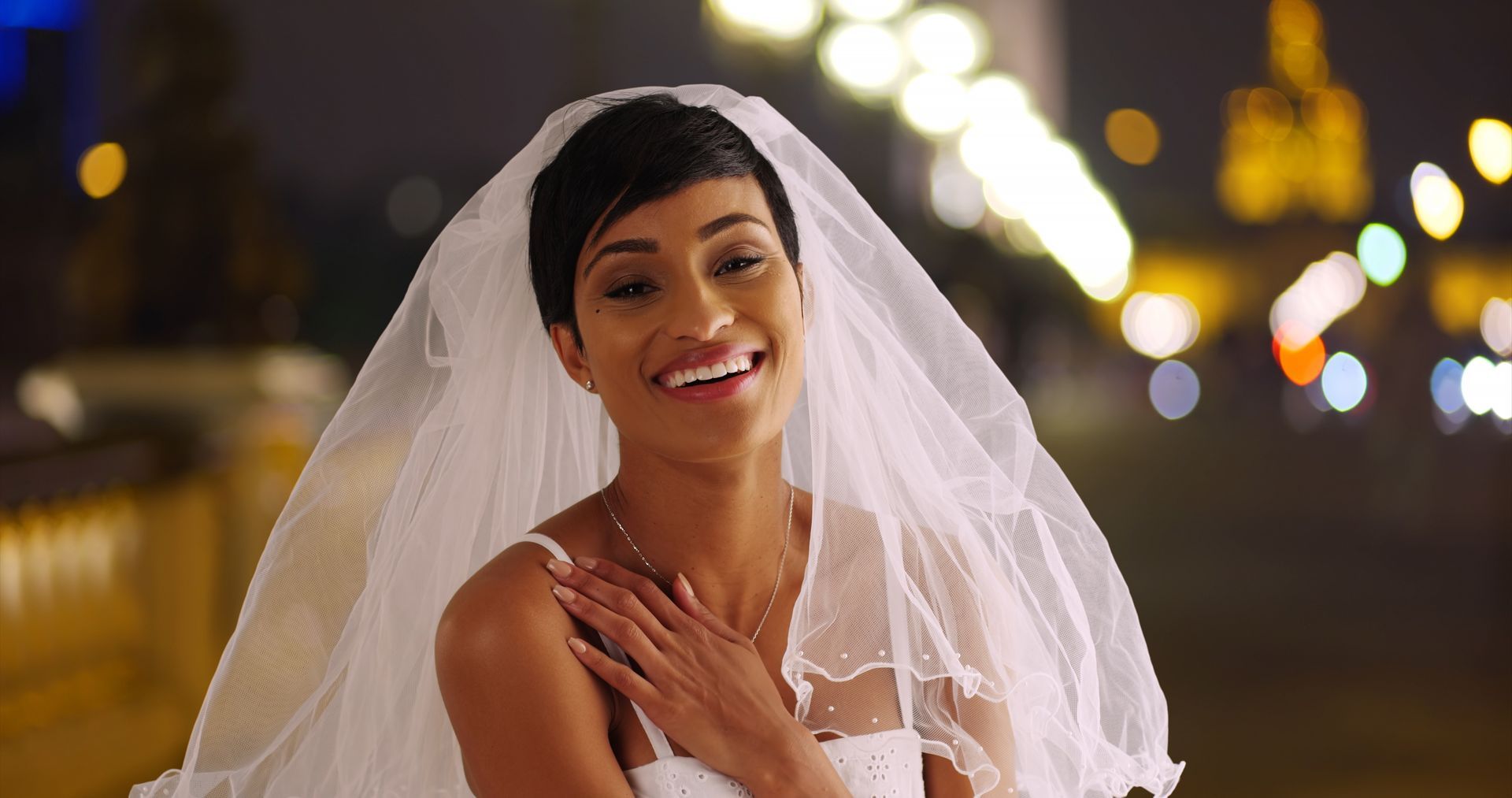 A bride in a wedding dress and veil is smiling at the camera.