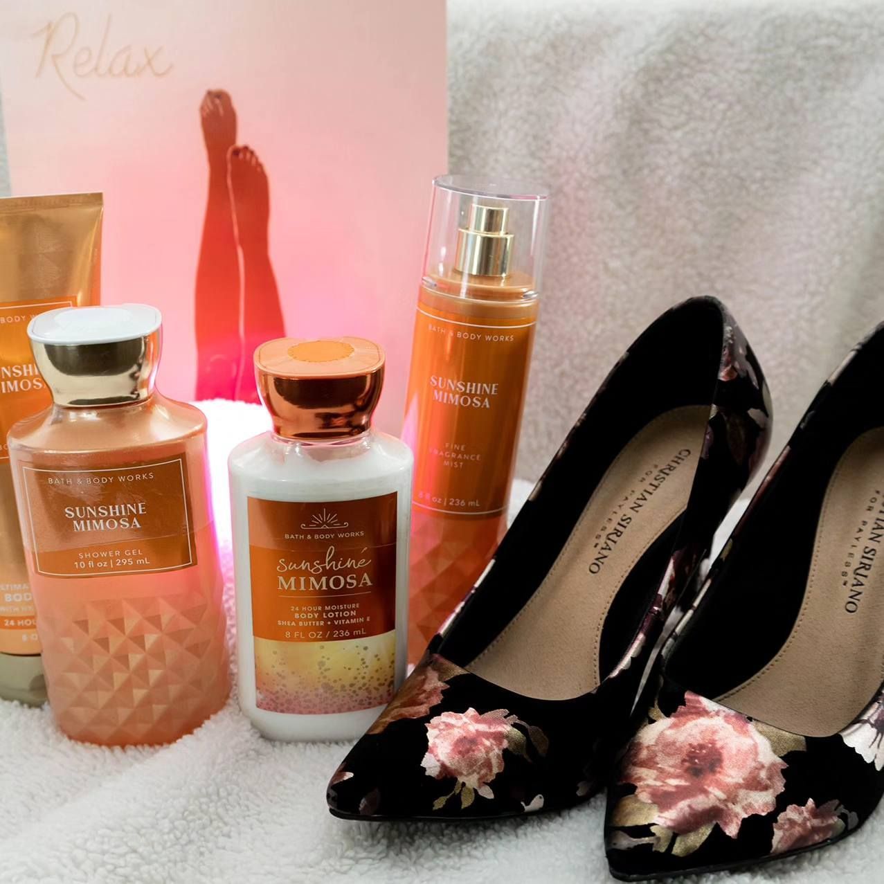 A pair of black shoes with flowers on them are surrounded by bottles of lotion and perfume