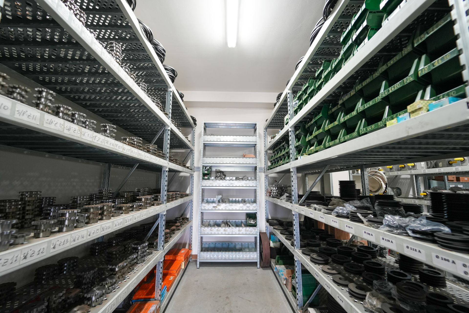 Uno stretto corridoio in un magazzino pieno di componenti industriali disposti su alte scaffalature metalliche.