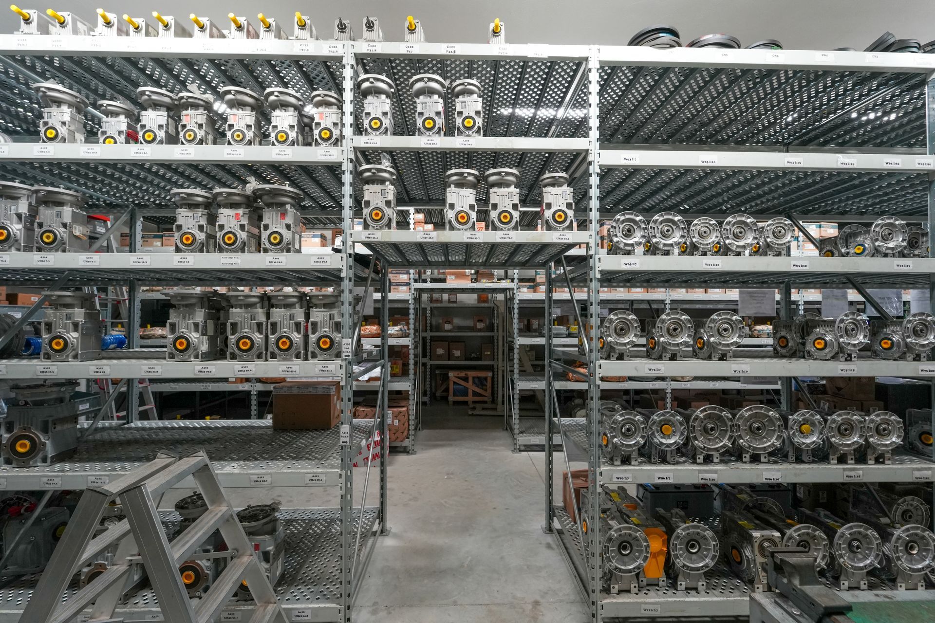 Scaffalature industriali in un magazzino, piene di numerose parti e componenti meccanici in metallo.